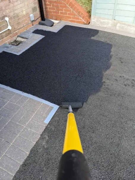 Tarmac being painted and sealed, showcasing a dramatic difference with one side appearing faded and worn, and the other restored.