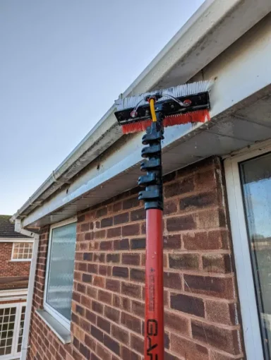 Water-fed pole cleaning a white gutter, effectively removing dirt and grime for a spotless and well-maintained appearance.