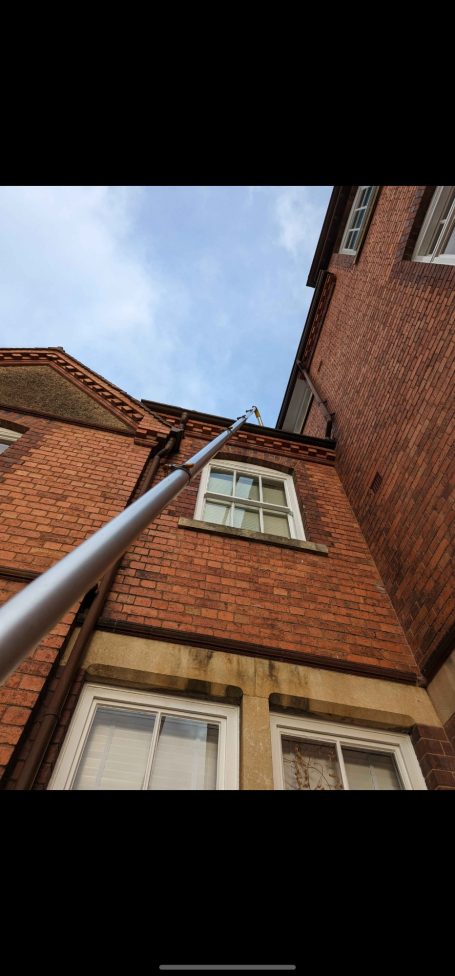 Gutter vac system reaching a tall three-storey building to efficiently clear debris from gutters.